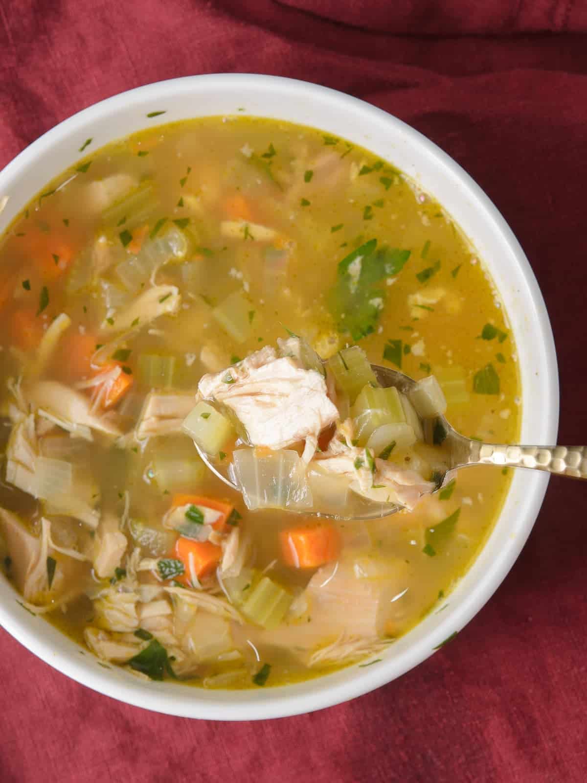turkey soup in a bowl with a spoon lifting out a bite showing the tender turkey meat and rich broth
