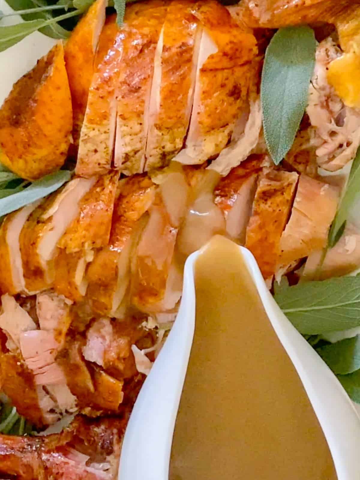 a platter of sliced thanksgiving turkey being dressed with gravy