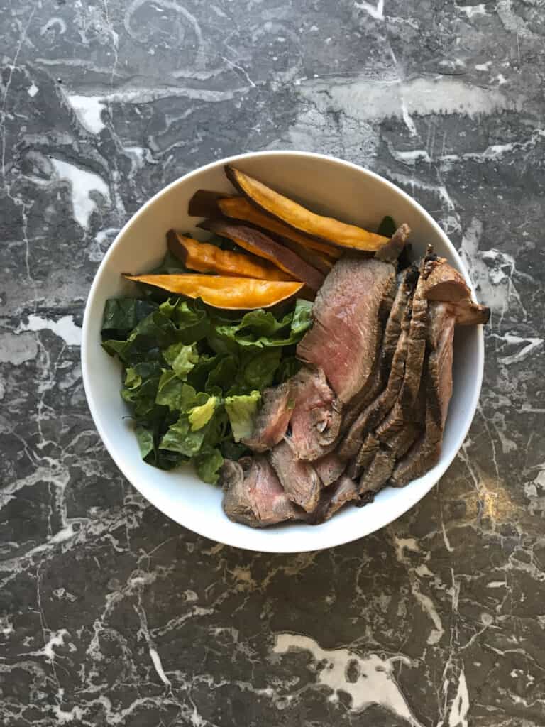 steak and sweet potato meal prep bowl with greens, steak and sweet potato fries.