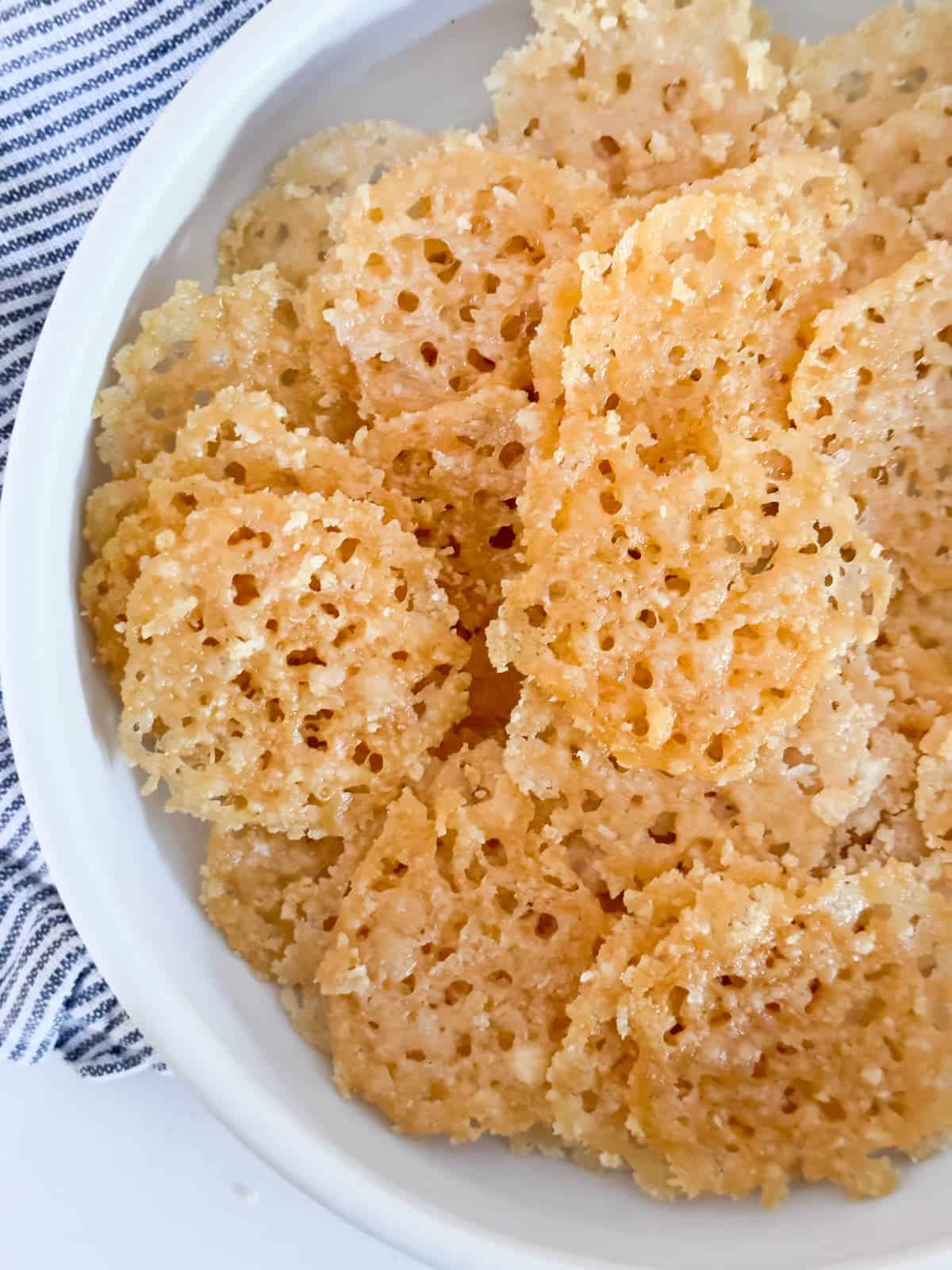 A bowl of crispy cheese crips crackers on a white table.